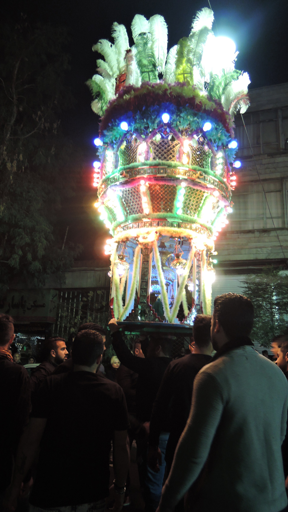 夜の路上行進で担がれる、光に彩られた宗教的装飾物